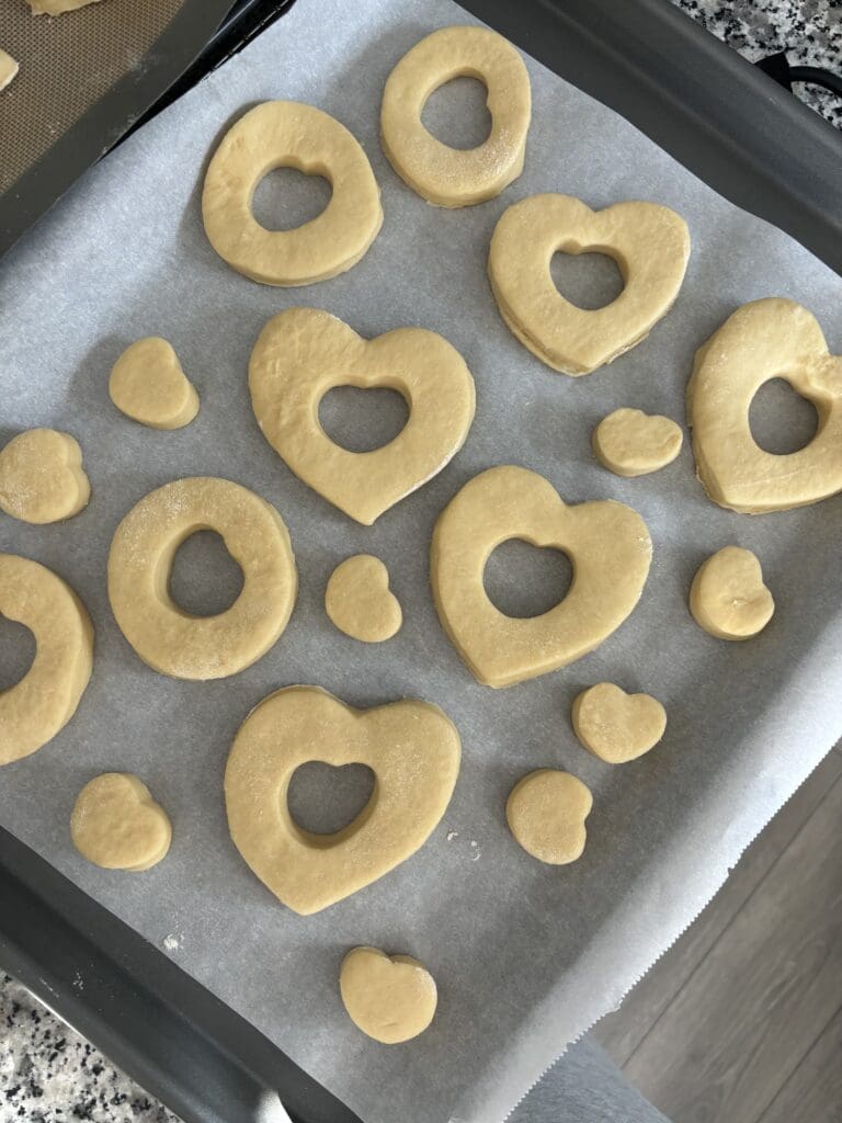 heart shaped donuts arranged on baking tray, rising